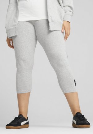 Grijze cropped leggings met een gladde textuur en een klein zwart logo aan de zijkant, gecombineerd met zwarte sneakers met een witte accente.
