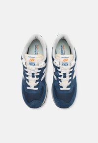 Navy blue sneakers with suede and mesh materials, white accents, and contrasting laces. Features an "NB Classic 574" label.