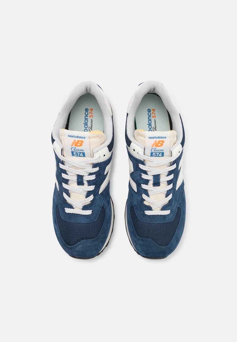 Baskets bleu marine en matériaux en daim et en maille, avec des accents blancs et des lacets contrastés. Présente une étiquette "NB Classic 574".