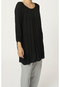 Un haut noir à manches longues en tissu léger, avec un col rond, un design plissé et un détail de bouton à l'avant. Assorti avec un pantalon gris clair.