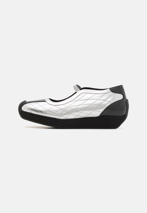 Silver quilted slip-on shoe with black accents, rounded toe, and soft rubber sole. Features a flexible design and minimal stitching details.