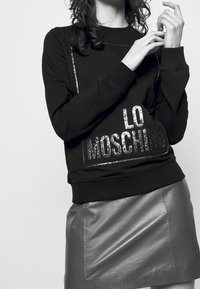 Černá mikina s metalickým logem "LO MOSCHINO", spárovaná s přiléhavou šedou koženou mini sukňou. Hladké materiály a moderní střih.