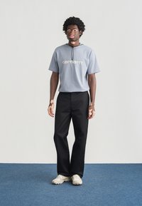 Ανοιχτό μπλε κοντομάνικο T-shirt με το λογότυπο "Carhartt", σε συνδυασμό με μαύρο παντελόνι και κρεμ αθλητικά παπούτσια. Λείο ύφασμα και άνετη εφαρμογή.