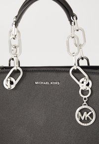 Sac à main en cuir noir texturé avec des accents de chaîne argentée, un porte-clés détachable rond et un logo de marque embossé à l'avant.