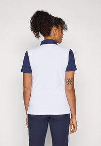 Πόλο μπλούζα κοντού μανικιού με ναυτικό γιακά και μανίκια, λευκό σώμα και λεία υφή. Διαθέτει ταμπελάκι στο στρίφωμα και τατουάζ στο αριστερό χέρι.