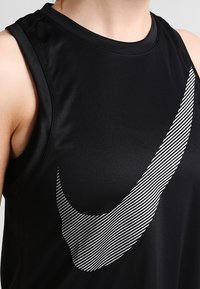 Canotta sportiva nera realizzata in tessuto liscio e traspirante, con un grande logo Nike a strisce bianche sul davanti.