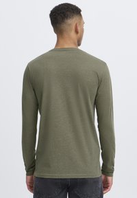 Langarmshirt in olivgrün, aus weichem Stoff gefertigt, mit Rundhalsausschnitt und lockerer Passform, minimalen Nähten.