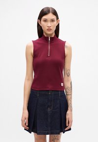Haut sans manches bourgogne avec un col haut et des détails de fermeture éclair argentés, associé à une jupe plissée en denim foncé. Tissu doux et extensible.