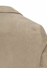 Beigefarbener Textil mit leichtem Glanz, der ein weiches gewebtes Muster und ein strukturiertes Schulterdesign aufweist.