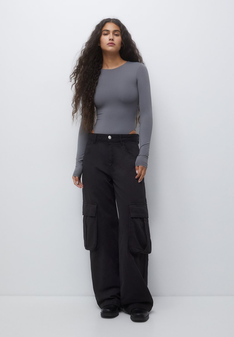 Body grigio a maniche lunghe con scollo rotondo abbinato a pantaloni cargo neri larghi con tasche laterali e chiusura a bottone.