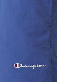 Kék sportnadrág könnyű anyagból, fehér "Champion" logóval hímzéssel, a "C" betűben egy kis piros kiegészítéssel.