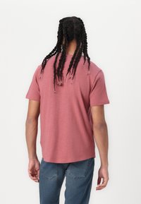 Korte mouwen, vervaagde rozenkleurige t-shirt met een ronde halslijn en een relaxte pasvorm, gecombineerd met blauwe jeans. De achterkant toont een gestructureerde stof.