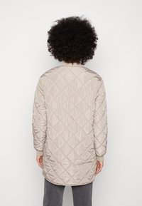 Ljusbeige kviltad jacka med diamantmönster, långärmad, med ribbade ärmslut och rundad halsringning. Slätt, glänsande tyg.