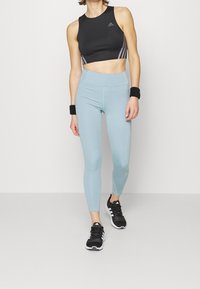 Top deportivo negro corto con logo gris, mallas de talle alto azul claro y zapatillas negras para correr con detalles en blanco. Muñequeras texturizadas.