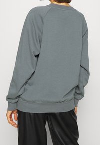 Šedá mikina s volným střihem, žebrovanými manžetami a lemem. Hladká textura, raglánové rukávy a jednoduchý design bez viditelných log.