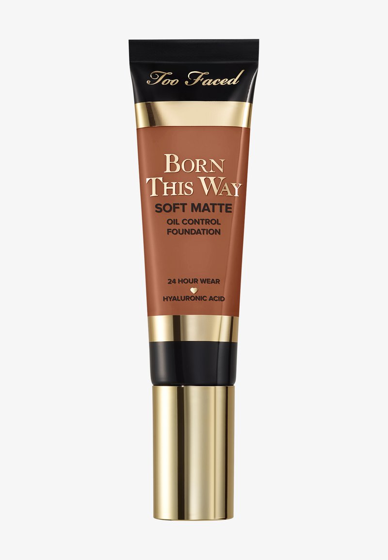 Tube compressible marron avec des accents dorés et noirs, étiqueté "Born This Way Soft Matte Oil Control Foundation," avec un capuchon à rabat.