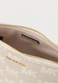 Pochette en toile beige avec motif de logo embossé, fermeture éclair dorée et un intérieur lisse et doublé comportant une étiquette.
