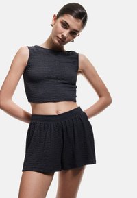 Top corto negro texturizado con cuello redondo, combinado con pantalones cortos de cintura alta que presentan una cinturilla elástica y un corte relajado.