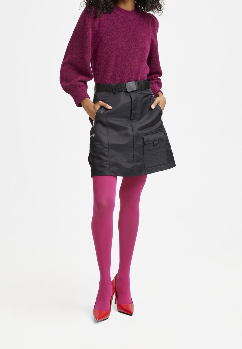 Pull en maille violet, mini-jupe en satin noir avec poches, collants roses et talons rouges. Doté d'une ceinture à la taille et d'une finition texturée.