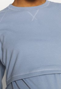 Felpa azzurra chiara realizzata in tessuto morbido, con scollatura rotonda, maniche raglan e dettagli decorativi ricamati.