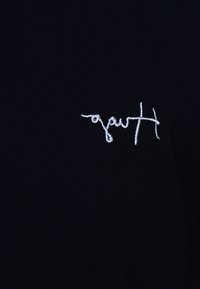 Mot en cursive brodé en blanc sur fond de tissu noir, orientation du texte ou formulation exacte incertaine.