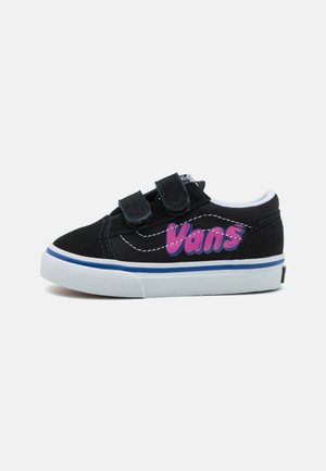 Baskets en toile noires avec des sangles Velcro, présentant des accents blancs et un logo violet sur le côté. Comprend une semelle en caoutchouc blanche avec des détails bleus.