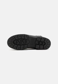 Black rubber boot outsole with deep tread for traction, featuring a textured surface and a smooth, solid center section.