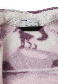 Fleece-stoff i lys rosa med lilla nyanser og abstrakt dyresilhuett. Har et merke med teksten "Jeg var her" og detaljer med svart stropp.