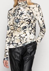 Lange mouw turtleneck top van zachte stof, met een meerkleurig spetterpatroon in beige, zwart en blauwe tinten. Gepaarde met zwarte leren broek.