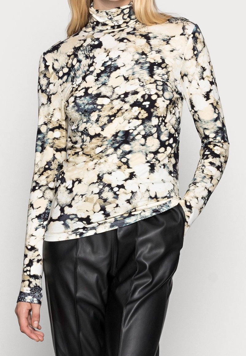Lange mouw turtleneck top van zachte stof, met een meerkleurig spetterpatroon in beige, zwart en blauwe tinten. Gepaarde met zwarte leren broek.