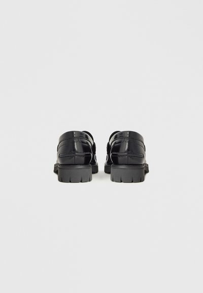 Czarne lakierowane skórzane buty o gładkim wykończeniu, zaokrąglonym nosku i grubej gumowej podeszwie z rowkami zapewniającymi przyczepność.