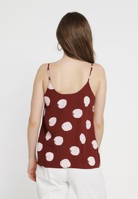 Camisola bordeaux con motivi circolari rosa pallido, spalline regolabili e vestibilità ampia. Tessuto liscio con una leggera trama.