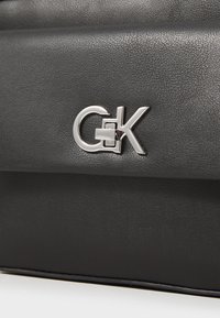 Borsa a mano in pelle nera con una texture, dotata di un logo metallico, caratterizzata da una forma rettangolare elegante e dettagli di cucitura sottili.