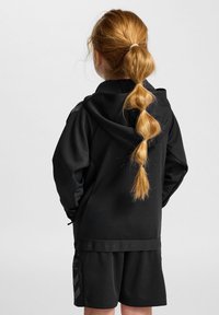 Svart hoodie med en texturerad yta, med en midjeresår. Matchad med svarta shorts som visar en logotyp och ett chevronmönster.