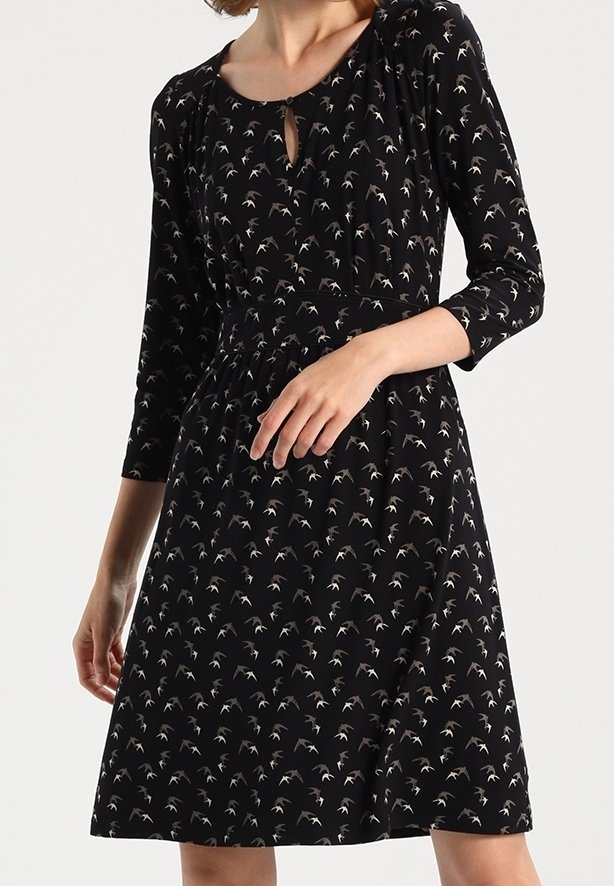 Robe noire avec un petit motif d'oiseaux blancs, manches trois-quarts, décolleté rond avec découpe en forme de goutte et taille cintrée.