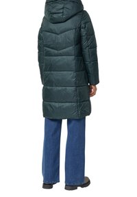 Ciemnozielona kurtka puchowa z kapturem, z pikowanym wzorem i długimi rękawami. W połączeniu z dżinsami o szerokich nogawkach i czarnymi botkami.