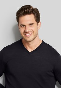 Schwarzer V-Ausschnitt-Pullover, feine Stricktextur, figurbetontes Design, Model lächelt, frisierte Haare, neutraler Hintergrund.