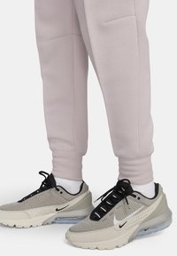 Sneaker Nike Air Max con tomaia in rete grigia chiara, con lacci neri, logo e un'unità d'aria visibile. Abbinati a pantaloni da jogging rosa chiaro.