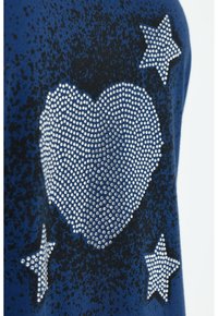 Un tessuto blu presenta un grande design a forma di cuore realizzato con strass argentati, circondato da due stelle, anch'esse decorate con strass.