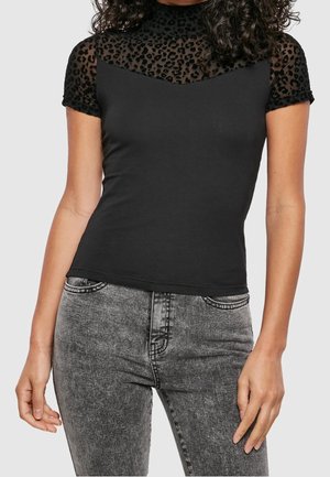 Kvinde iført en sort tætsiddende top med leopardmønstrede gennemsigtige korte ærmer kombineret med grå acid-wash højttaljede jeans.