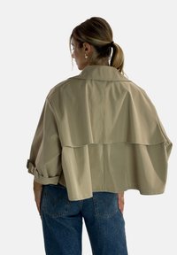 Jasnobeżowa krótka kurtka o warstwowej konstrukcji, z szerokim kołnierzem i podwiniętymi rękawami, zestawiona z niebieskimi, wysokim stanem dżinsami.