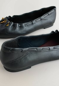 Fekete bőr balerinacipő texturált felülettel, hullámos szegéllyel és díszes arany díszítéssel az orrán. Puha belső bélés.