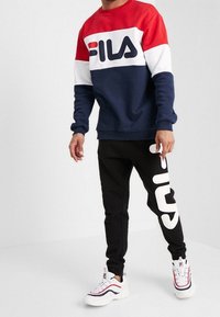 Felpa FILA a blocchi di colore rosso, bianco e blu navy con maniche lunghe; pantaloni jogger neri con un grande logo bianco; scarpe sportive casual.