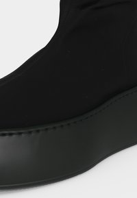 Κοντινή λήψη μαύρου παπουτσιού slip-on με παχύ πάτο πλατφόρμας και επάνω υλικό με λεία, ματ φινίρισμα.