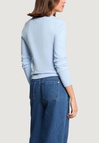 Jasnoniebieski dziany sweter z okrągłym dekoltem i prążkowanymi mankietami, zestawiony z wysokim stanem niebieskich dżinsów z tylnymi kieszeniami.