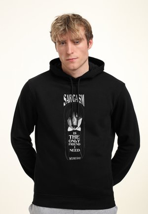 Jongen met blond haar draagt een zwarte hoodie met een gestileerd meisje met zwart haar en de tekst "Sarcasme is de enige vriend die ik woensdag nodig heb."