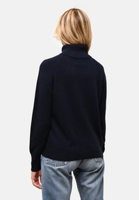 Ciemnoniebieski sweter z golfem wykonany z miękkiej dzianiny. Ma żeberkowy kołnierz i mankiety, lekko luźny krój, zestawiony z jasnoniebieskimi dżinsami.