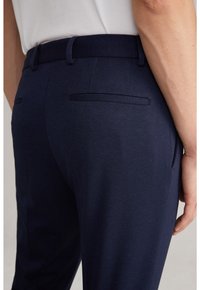 Dunkelblaue Hosen mit strukturierter Oberfläche, ausgestattet mit einem flachen Bund, zwei aufgesetzten Gesäßtaschen mit flachen Verschlüssen und einer taillierten Passform.