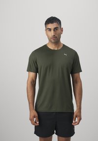 Camiseta atlética de color verde oliva en tejido ligero con acabado texturizado, que presenta un pequeño logo blanco en el pecho y cuello redondo.