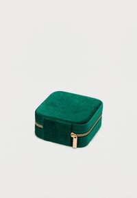 Kis négyzet alakú zöld velúr ékszerdoboz arany cipzárral és húzófüllel, zárva, egyszínű világos háttéren.